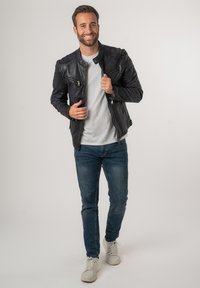 Zwarte leren jack met ritszakken, gestructureerde schouders en een getailleerd ontwerp, gedragen over een lichtgrijs t-shirt en blauwe jeans.