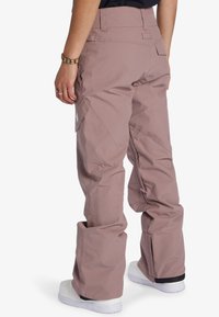 Rosa Snowboardhosen mit lockerer Passform, ausgestattet mit Cargo-Taschen, verstellbaren Säumen und einer glatten Textur. Die Rückansicht zeigt die Details der Nähte.