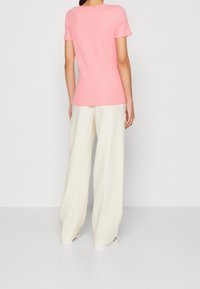 T-shirt rosa a maniche corte a coste abbinato a pantaloni bianchi larghi. Tessuto morbido con una silhouette aderente e scollo rotondo.