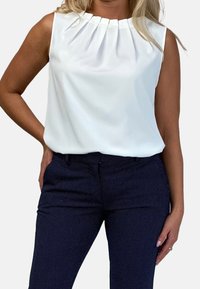 Vit ärmlös blus med veck vid halslinningen, kombinerad med marinblå byxor med prickar. Slät tygkvalitet med avslappnad passform.