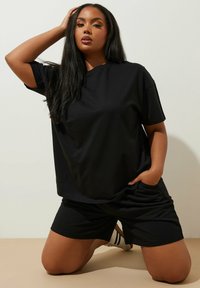 Svart bomullst-shirt och shorts-set med en lös passform. T-shirten har en rund halsringning; shortsen har sidofickor. Slät textur.