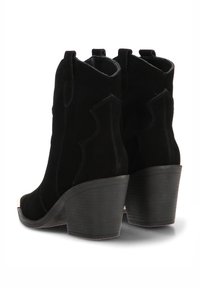 Botas de tobillo de ante negro con costuras decorativas, punta afilada y un tacón de goma grueso. Incluyen tiradores para facilitar su uso.