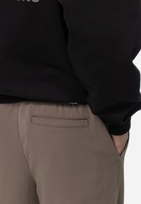 Sweatshirt noir avec des poignets côtelés, associé à un pantalon beige avec un détail de poche arrière. Texture lisse et coupe décontractée.