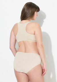 Beige naadloze bh en set met hooggesneden ondergoed. Zachte, gladde textuur met een ronde rug en minimalistisch ontwerp. Geen zichtbare aansluitingen.