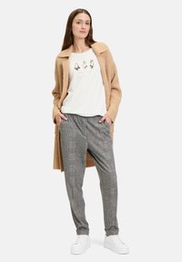 Beige ribbet cardigan over en hvid skjorte med trykte detaljer, parret med gråternede bukser og hvide sneakers.