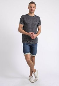 T-shirt gris foncé à manches courtes avec bordure blanche, associé à un short en denim avec ourlet retroussé et des baskets blanches. Tenue simple et décontractée.