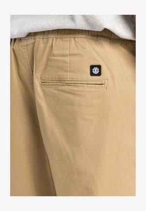 Beige bomuldsshorts med elastisk talje, baglomme med en horisontal søm og et sort logo-patch på lommen.