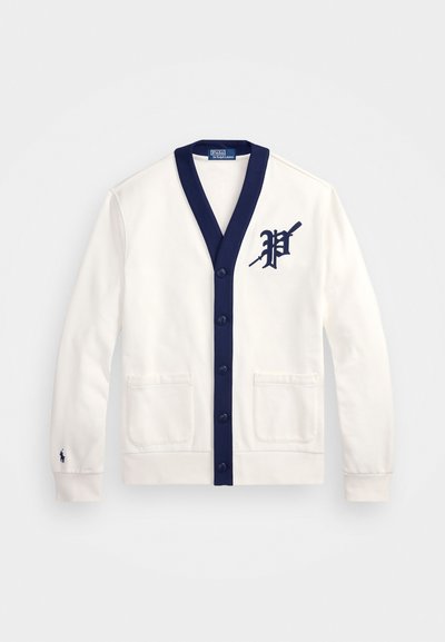 Vit cardigan med marinblå detaljer, v-ringning, knäppning framtill, två framfickor, med en stor marinblå "P"-logotyp på vänster sida.