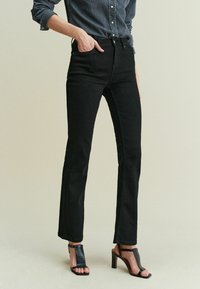 Sorte højtaljede jeans med en lige ben-design, lavet af denim. Kombineret med sorte hælsandaler med et struktureret, krokodillepræget mønster.