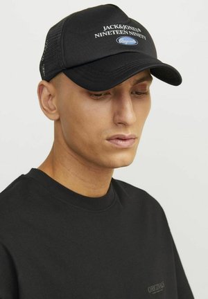 Gorra negra con visera curva y paneles de malla. Presenta el logo "JACK&JONES NINETEEN NINETY" y acentos azules. Se lleva con una camiseta negra.