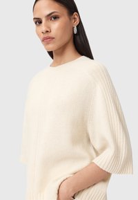 Maglione lavorato a maglia color crema con un fit rilassato, caratterizzato da texture a coste sulle maniche e sul corpo, e spalle scese.