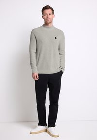 Světlý šedý žebrovaný svetr s vysokým límcem a černými akcenty, doplněný černými kalhotami a bílými sneakers. Jednoduchý, moderní design.