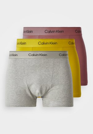Drei Paare Calvin Klein Boxershorts in Grau, Gelb und Burgunderrot. Jede hat einen kontrastierenden Bund mit dem Markennamen in gedrucktem Schwarz.