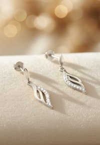 Silberne Ohrringe mit einem drehenden Design, verziert mit kubischen Zirkonia, in einer länglichen Form und mit einem polierten Finish auf einer sanften beigen Oberfläche.