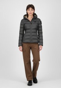 Dunkelgraue Steppjacke mit taillierter Silhouette und Kapuze, ausgestattet mit einem Reißverschluss und dezentem Branding. Kombiniert mit braunen Cargo-Hosen und schwarzen Stiefeln.