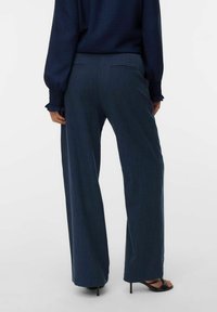 Vidbyxor i mörkblått tyg, med platt framsidan, två fickor och en jämn yta, ihop med svarta högklackade sandaler.