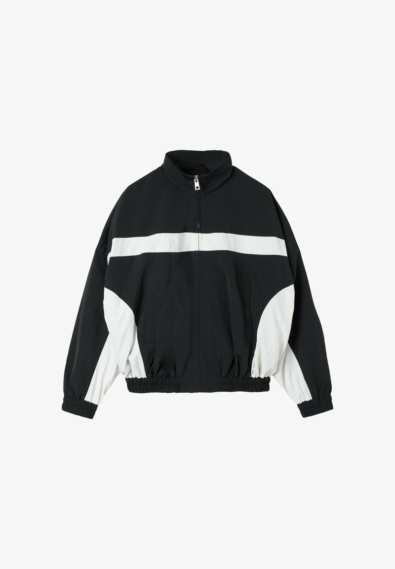 Veste coupe-vent zippée noir et blanc avec une bande blanche horizontale sur la poitrine et des panneaux blancs sur les manches. Poignets et ourlet élastiques.