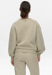 Sudadera gris claro con mangas holgadas, puños y bajo acanalados. Tejido de mezcla de algodón suave. Diseño minimalista con una pequeña etiqueta en la parte trasera.