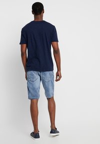 Camiseta de manga corta en color navy combinada con pantalones cortos de mezclilla azul claro, con bolsillos traseros y un corte relajado. Calzado casual completa el conjunto.