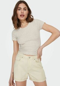 Lys beige ribbet t-skjorte med kort erm og bølgete kanter, kombinert med lysegule høy midje denimshorts, med rullet opp mansjetter og lommer.