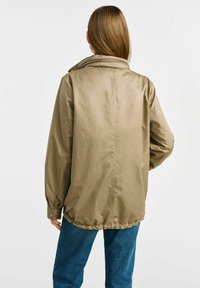 Kahaki kurtka o swobodnym kroju, z wysokim kołnierzem, elastycznym dołem i długimi rękawami. Wykonana z gładkiego, lekkiego materiału.