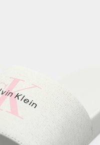 Sandal in gomma bianca texturizzata di Calvin Klein con logo rosa "CK" e nome del marchio nero sulla fascia, su uno sfondo semplice.