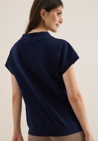 Haut à manches courtes bleu marine avec une coupe décontractée et un ourlet côtelé. La texture lisse et le détail du col retroussé renforcent son design décontracté.