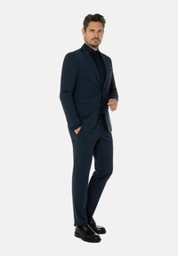 Marineblauw pak met een slim fit ontwerp, voorzien van een enkele knoopsluiting en geknipte revers. Gecombineerd met een zwart dresshemden en glanzende zwarte schoenen.