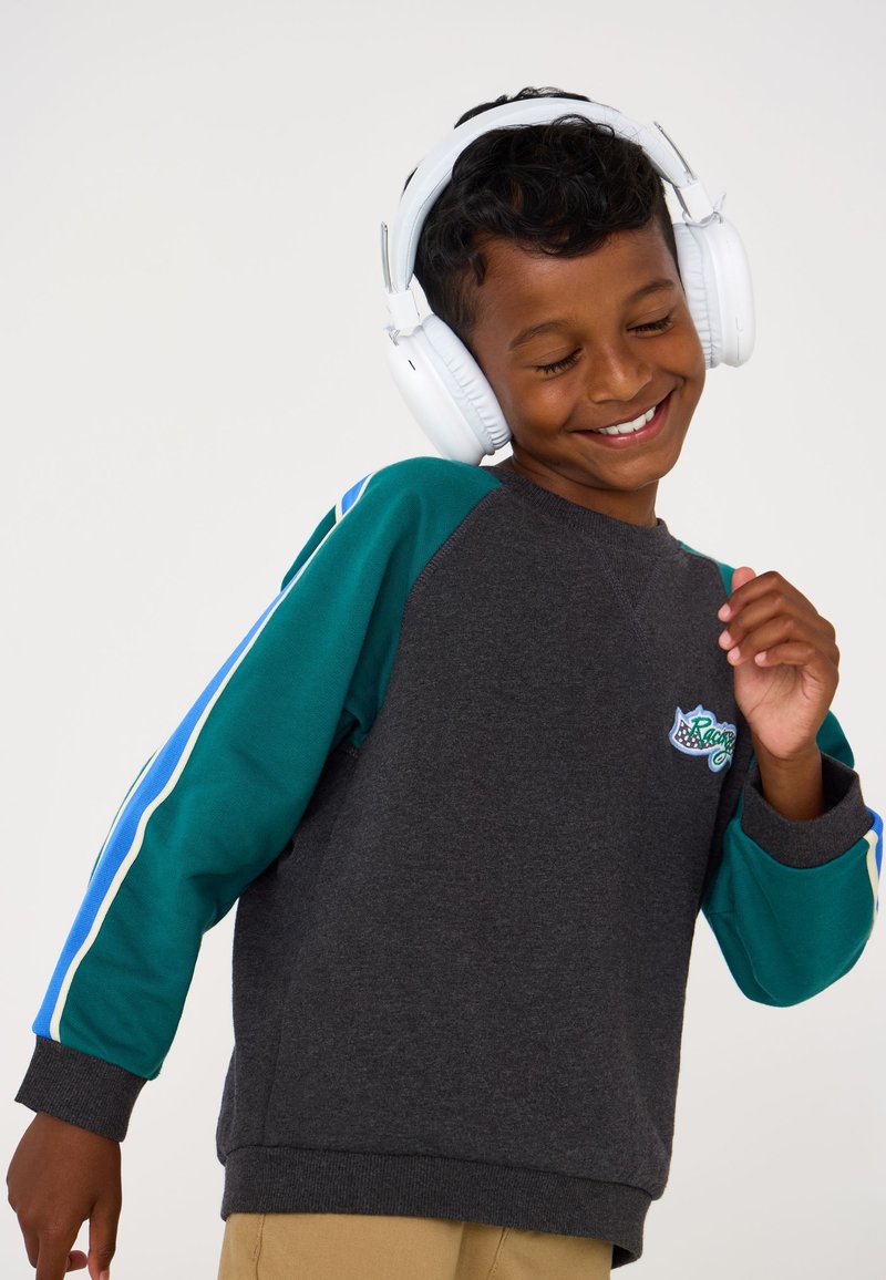 Grauer Sweatshirt mit türkisen und blauen Streifenakzenten. Verfügt über ein buntes, besticktes Logo auf der Brust. Getragene weiße Over-Ear-Kopfhörer.