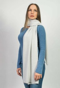Lys grå tørklæde lavet af blødt stof, draperet løst omkring halsen, parret med en blå langærmet skjorte og jeans.