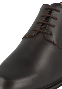 Bruine leren geklede schoen met een gladde textuur, ronde neus en vier veterogen. Beschikt over contrasterende stiksels en een slanke zool.
