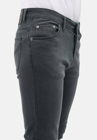 Donkergrijze denim jeans met een slim fit, voorzien van zilverkleurige beslag, vijf zakken en een subtiele gewassen textuur aan de voorkant.