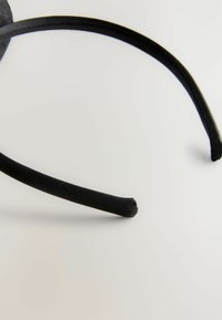 Zwart stoffen haarband met een gladde textuur, licht gebogen vorm en een klein rafelig uiteinde. Simpel en minimalistisch ontwerp.