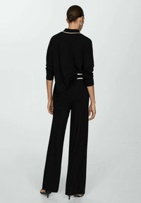 Haut en tricot noir avec un col blanc et des détails rayés, associé à un pantalon noir à jambes larges. Texture lisse et coupe décontractée.