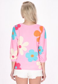 Top rosa a maniche lunghe con grandi motivi floreali multicolori in blu, arancione e crema. Presenta maniche a sbuffo e un colletto rotondo.