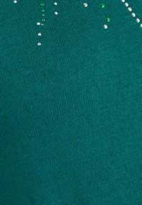 Suéter de punto en color teal con una textura suave y adornos decorativos de cristal de varios tamaños, dispuestos verticalmente.