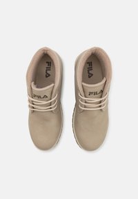 Beige tenisky Fila s hladkým svrškem, kulatou špičkou, šněrováním a měkkou podšívkou viditelnou uvnitř. Podešev je strukturální pro lepší přilnavost.