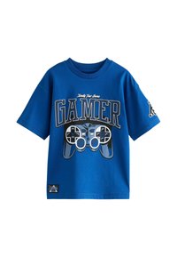 T-shirt in cotone blu con testo "GAMER" in bianco e nero e una grafica di un controller di gioco. Design a maniche corte e colletto rotondo.
