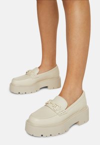 Crème leren platform schoenen met een chunky zool, voorzien van een decoratieve strap en metallic accenten. Glad textuur en rond toelont ontwerp.