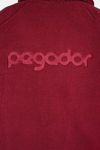 Burgundi värvi fliisjakk, millel on reljeefne "pegador" logo. Kangas on pehme, tekstuuriga pinnaga ja ühtlase sügava värvusega.