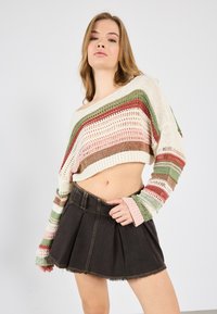 Häkelstrickpullover mit mehrfarbigen Streifen, schulterfreies Design; kombiniert mit einem schwarzen Denim-Rock mit ausgestelltem Schnitt und fransigem Saum.