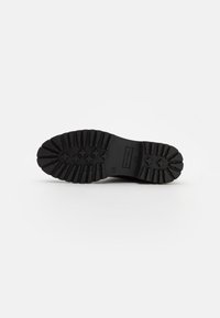 Semelle de chaussure en caoutchouc noir avec des motifs de semelle profonds, présente des détails de marque et des éléments de traction robustes ; conçue pour la durabilité et l'adhérence.