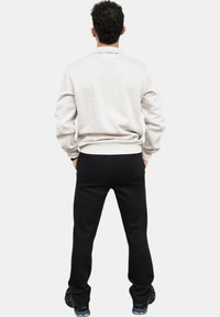 Conjunto masculino que presenta una sudadera gris claro con puños acanalados y pantalones negros. Los pantalones son ajustados y el modelo lleva zapatillas negras.