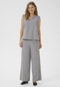 Ensemble bicolore rayé gris et blanc ; top sans manches avec accents en volants et pantalon large. Texture douce, coupe décontractée. Chaussures noires.