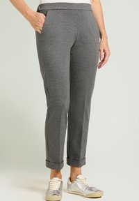 Pantalones grises de corte cónico hechos de tela suave, con bolsillos laterales y puños remangados, combinados con zapatillas metálicas.