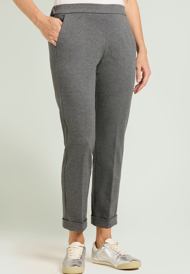 Pantalones grises de corte cónico hechos de tela suave, con bolsillos laterales y puños remangados, combinados con zapatillas metálicas.