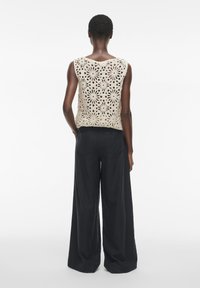 Top sin mangas de color beige a ganchillo con patrones de corte floral, combinado con pantalones sueltos de pierna ancha en una tela suave.