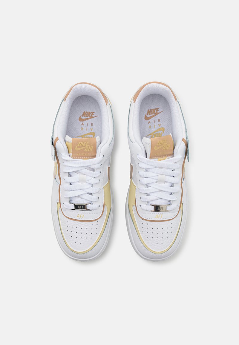 Zapatillas de piel blancas con acentos en amarillo claro y marrón, con una caja de dedos perforada, cordones planos y plantillas con marca.