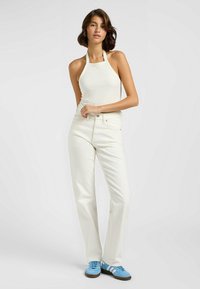Jeans rectos blancos combinados con un top halter ajustado en crema y zapatillas deportivas azules con rayas blancas. Tejido suave con hardware mínimo.