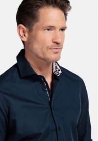 Chemise bleu marine à manches longues avec un col à motif floral, présentant une coupe standard et une texture de tissu lisse, conçue pour un usage décontracté.